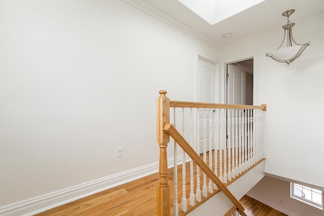 corridor with a skylight, wood finished floors, an upstairs landing, baseboards, and crown molding