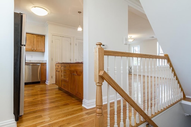 hall with light wood finished floors, baseboards, ornamental molding, and an upstairs landing