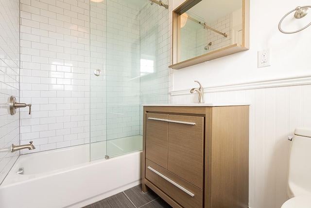 bathroom featuring toilet, a wainscoted wall, bath / shower combo with glass door, vanity, and tile patterned floors