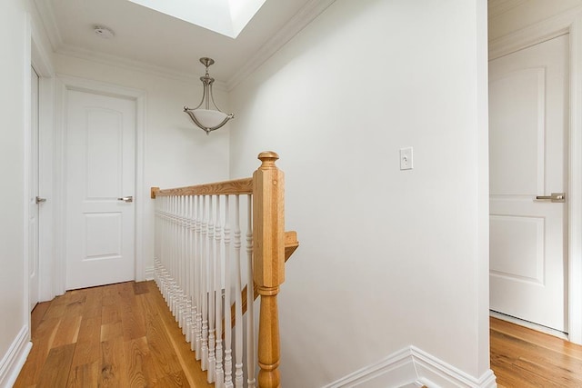 corridor with a skylight, light wood-style flooring, crown molding, and an upstairs landing