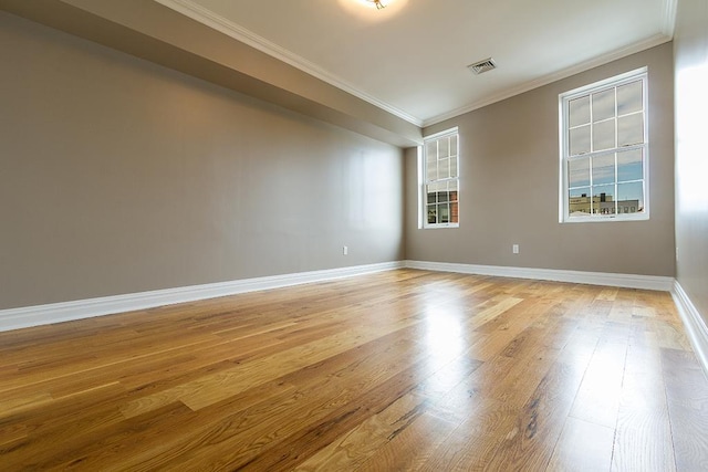 empty room featuring light wood finished floors, ornamental molding, visible vents, and baseboards