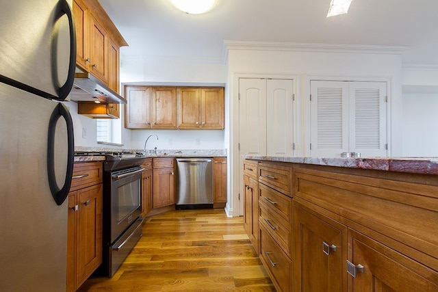 kitchen with crown molding, stainless steel appliances, brown cabinetry, and under cabinet range hood