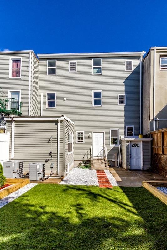 rear view of house with central air condition unit, a lawn, and entry steps