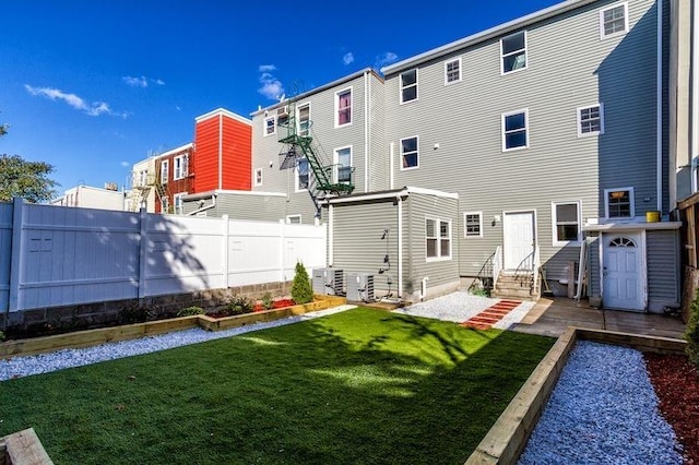 back of property featuring entry steps, a vegetable garden, central AC unit, a lawn, and fence