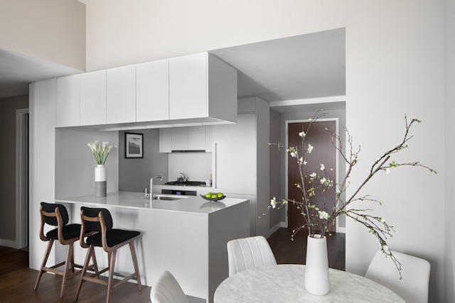 kitchen with kitchen peninsula, white cabinetry, sink, and dark hardwood / wood-style floors