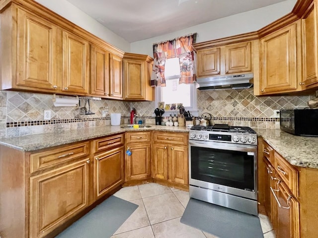 kitchen with stainless steel range with gas stovetop, under cabinet range hood, black microwave, light tile patterned flooring, and light stone counters