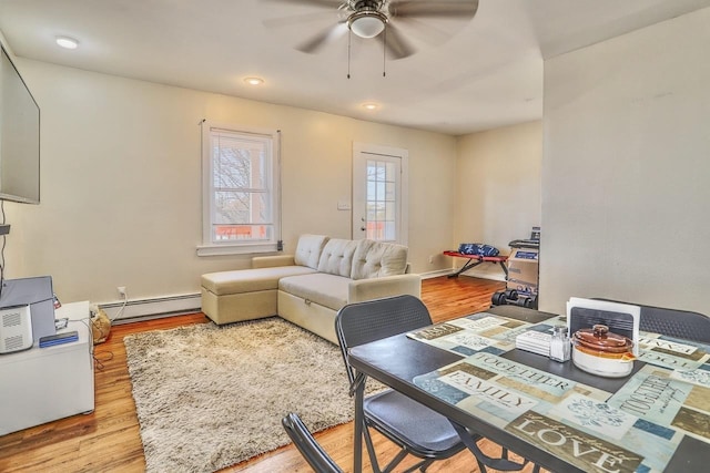 living room with light wood-style floors, a baseboard heating unit, and a ceiling fan