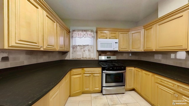 kitchen featuring white microwave, light tile patterned floors, light brown cabinetry, gas range, and dark countertops
