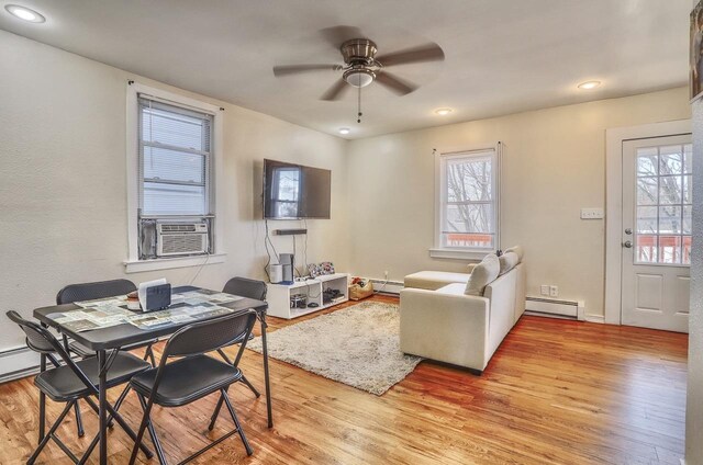living area featuring a baseboard radiator, light wood-type flooring, a ceiling fan, and cooling unit