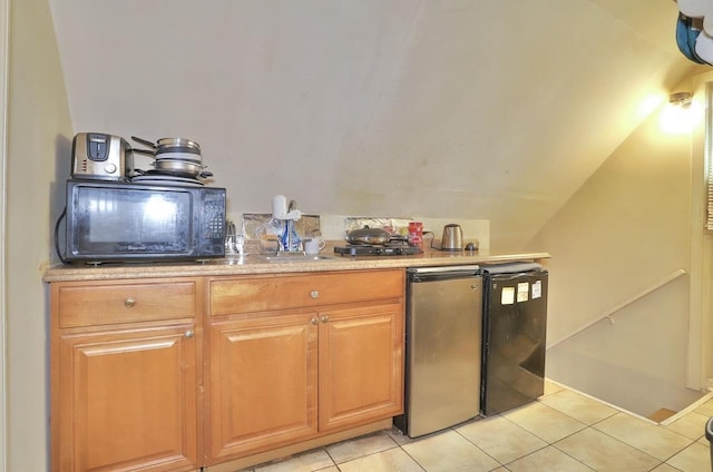 kitchen with light tile patterned flooring, light countertops, fridge, and vaulted ceiling