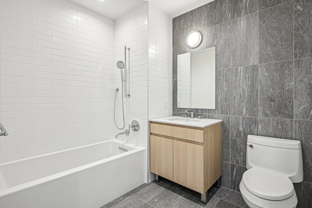 full bathroom with vanity, toilet, tiled shower / bath, and tile walls