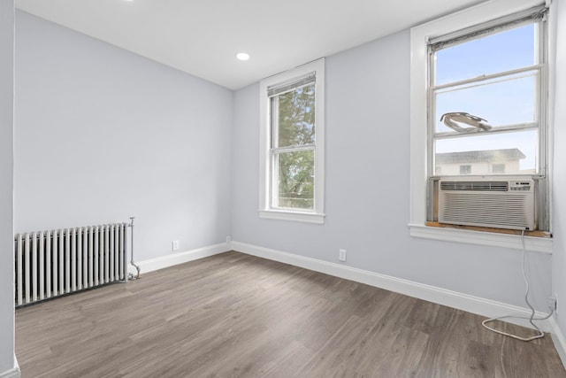 empty room featuring cooling unit, baseboards, radiator, and wood finished floors