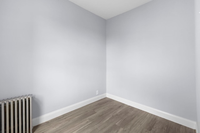 empty room featuring radiator heating unit, wood finished floors, and baseboards