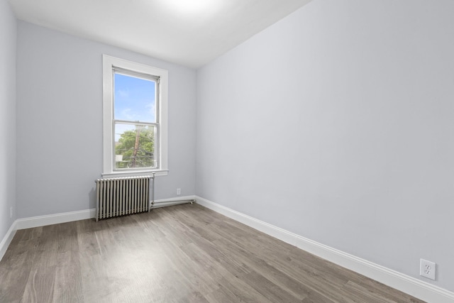 empty room featuring baseboards, radiator, and wood finished floors