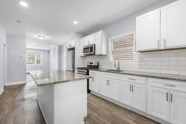 kitchen featuring dark wood-type flooring, a sink, white cabinetry, stainless steel appliances, and dark stone counters