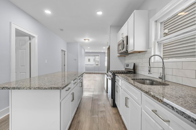 kitchen featuring a sink, tasteful backsplash, a kitchen island, stainless steel appliances, and light wood finished floors