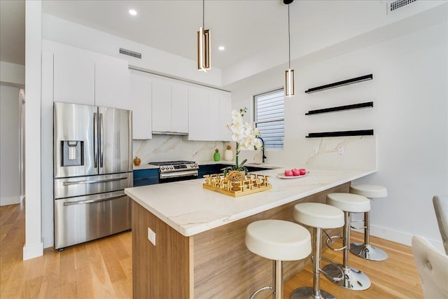 kitchen with light wood finished floors, tasteful backsplash, appliances with stainless steel finishes, a peninsula, and a kitchen bar