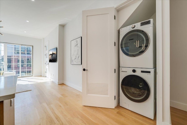 clothes washing area with laundry area, light wood-type flooring, stacked washing maching and dryer, and baseboards