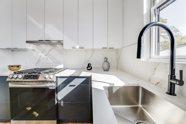 kitchen featuring stainless steel gas stove, a sink, backsplash, and white cabinetry