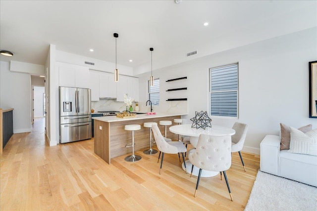 kitchen with light wood finished floors, tasteful backsplash, white cabinetry, a peninsula, and stainless steel fridge with ice dispenser