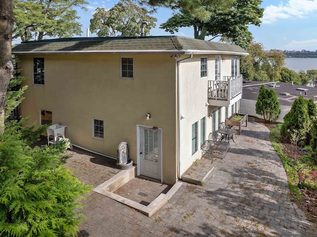 back of property with a balcony, a patio area, and a water view