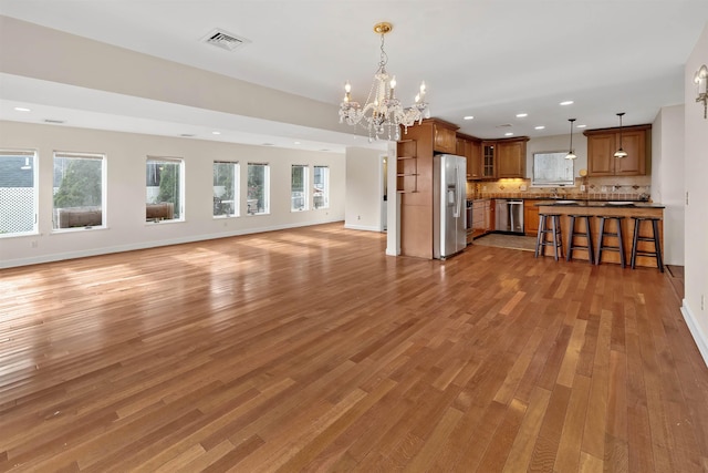 unfurnished living room featuring sink, light hardwood / wood-style floors, and an inviting chandelier