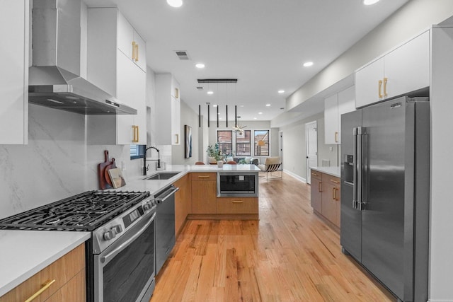 kitchen with a sink, a peninsula, modern cabinets, stainless steel appliances, and wall chimney range hood