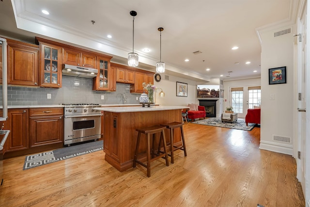 215 Monroe St Unit 3, Hoboken, NJ 07030 - kitchen featuring premium range, under cabinet range hood, brown cabinets, light countertops, and ornamental molding