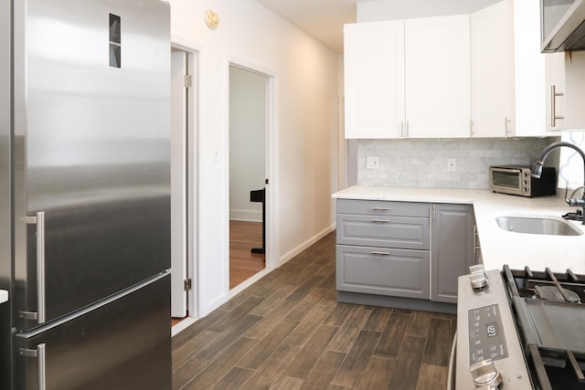 kitchen with appliances with stainless steel finishes, a sink, gray cabinets, wood finish floors, and backsplash