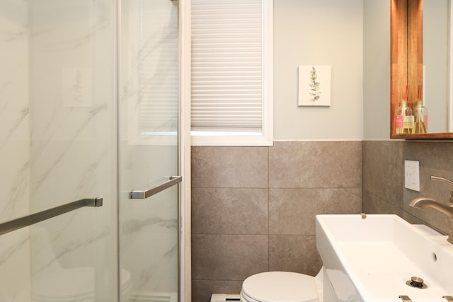 full bathroom featuring a sink, a marble finish shower, toilet, and tile walls