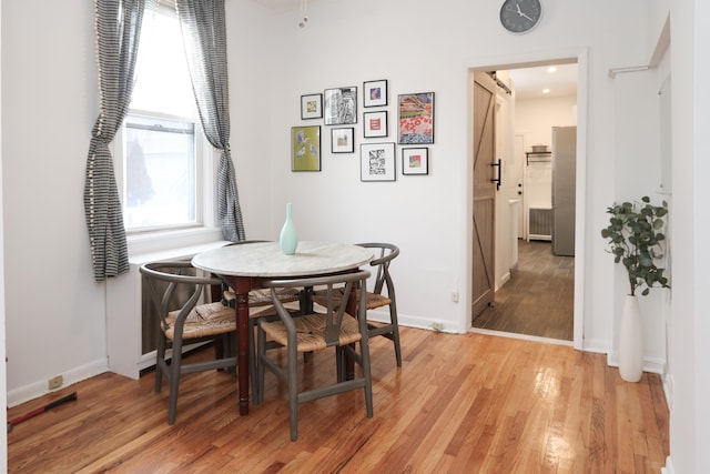 dining room featuring light wood finished floors, a barn door, and baseboards