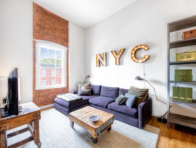 living area with wood finished floors, baseboards, and brick wall