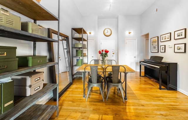 dining space featuring a towering ceiling, light wood-style floors, and baseboards