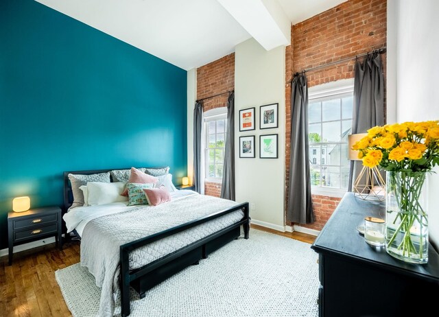 bedroom featuring brick wall, multiple windows, wood finished floors, and baseboards