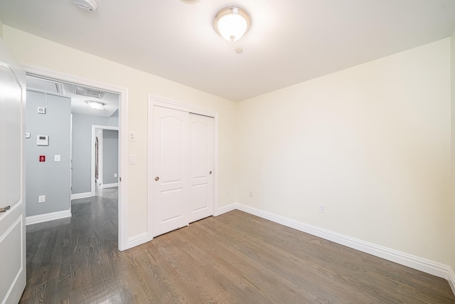 unfurnished bedroom with dark wood finished floors, a closet, attic access, and baseboards