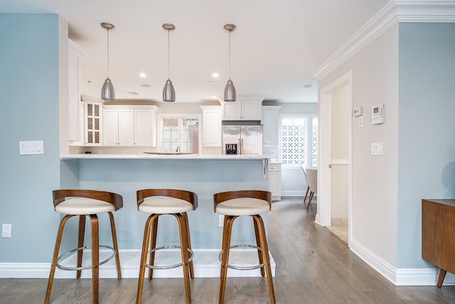 kitchen with a kitchen bar, dark wood-type flooring, white cabinetry, a peninsula, and stainless steel fridge with ice dispenser