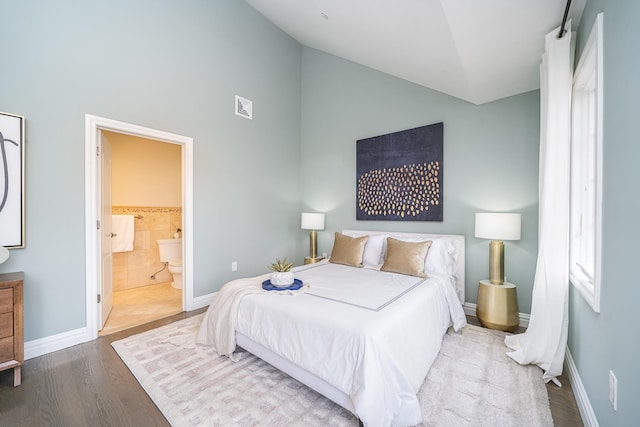 bedroom with wood finished floors, visible vents, baseboards, lofted ceiling, and ensuite bathroom