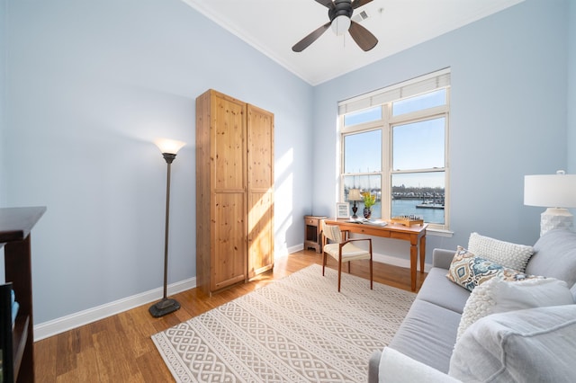 office area featuring baseboards, light wood-style flooring, ornamental molding, ceiling fan, and a water view