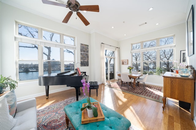 living area with wood finished floors, baseboards, recessed lighting, ornamental molding, and a water view