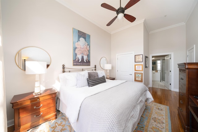 bedroom with ensuite bathroom, wood finished floors, crown molding, baseboards, and ceiling fan