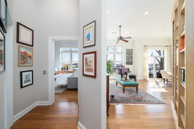 hallway featuring recessed lighting, baseboards, light wood-type flooring, and a towering ceiling