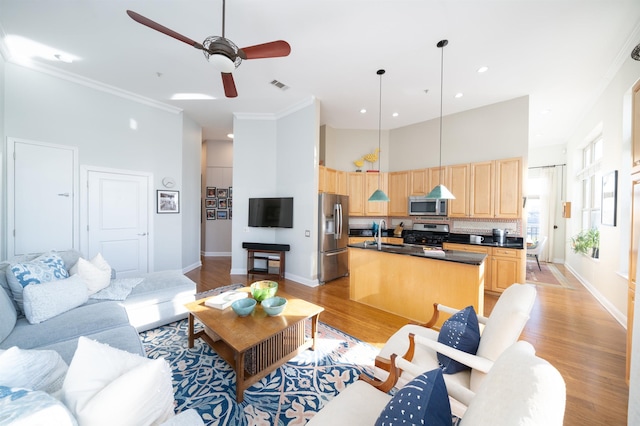 living area featuring light wood finished floors, visible vents, a high ceiling, and baseboards