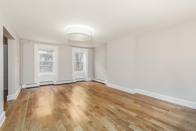 unfurnished room featuring wood finished floors, baseboards, and a baseboard radiator