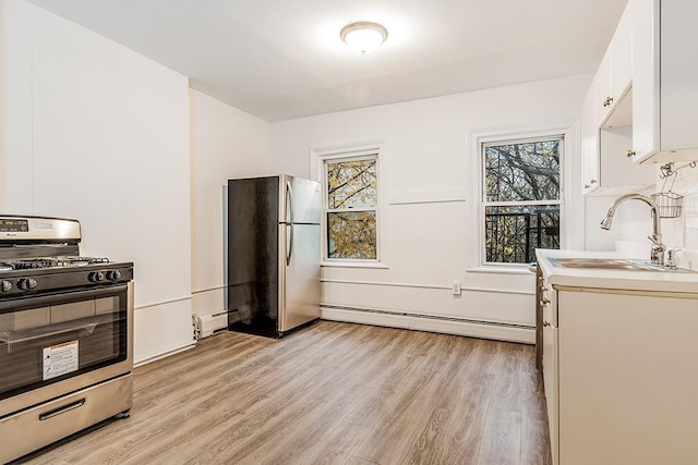 kitchen with light wood-type flooring, baseboard heating, appliances with stainless steel finishes, white cabinetry, and a sink