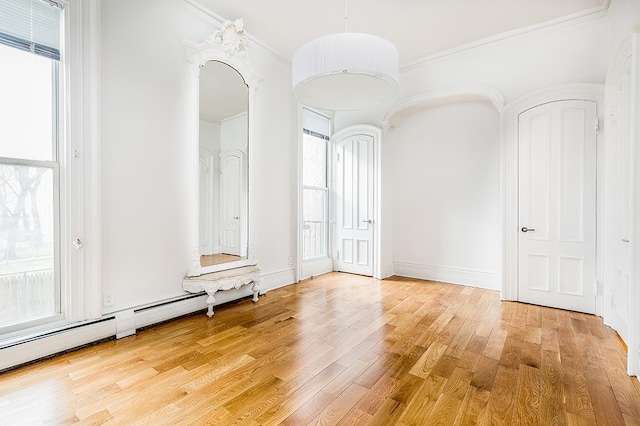 spare room featuring crown molding, baseboards, light wood-type flooring, and a baseboard radiator