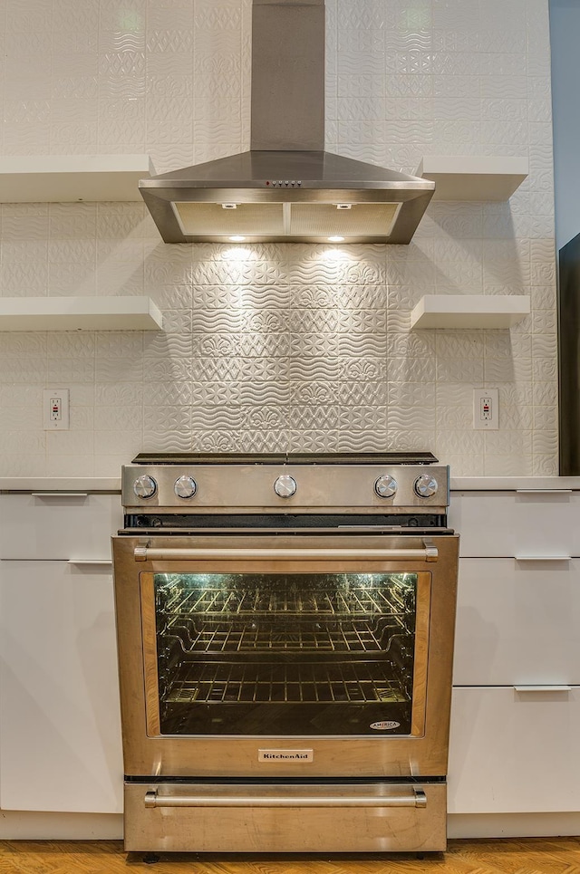 room details with open shelves, wall chimney range hood, stainless steel range with electric stovetop, and light countertops