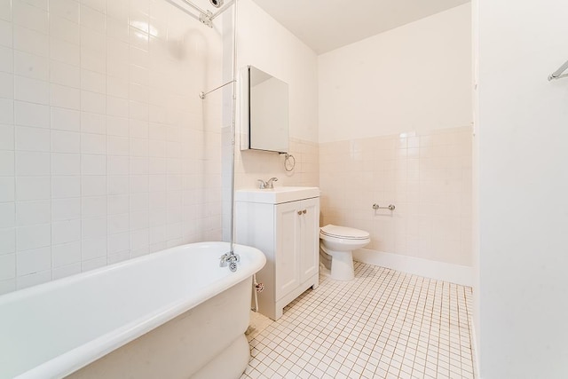 bathroom with tile patterned floors, toilet, tile walls, a soaking tub, and vanity