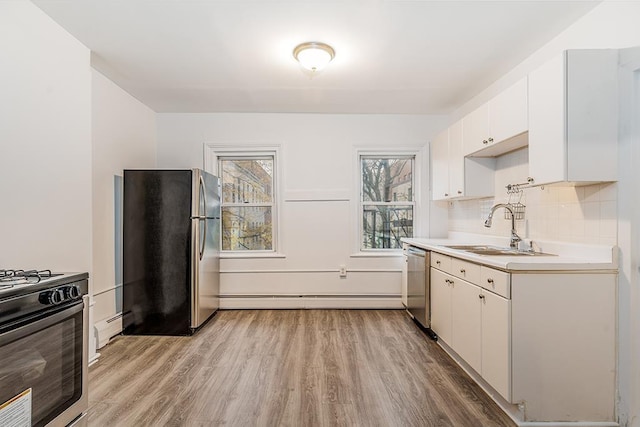 kitchen with a baseboard radiator, a sink, light wood-style floors, appliances with stainless steel finishes, and a baseboard heating unit