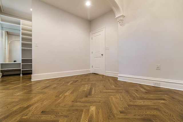 unfurnished room featuring arched walkways, a baseboard heating unit, baseboards, and decorative columns