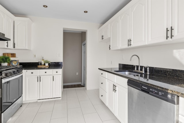 kitchen featuring dark stone countertops, appliances with stainless steel finishes, light tile patterned floors, white cabinets, and sink